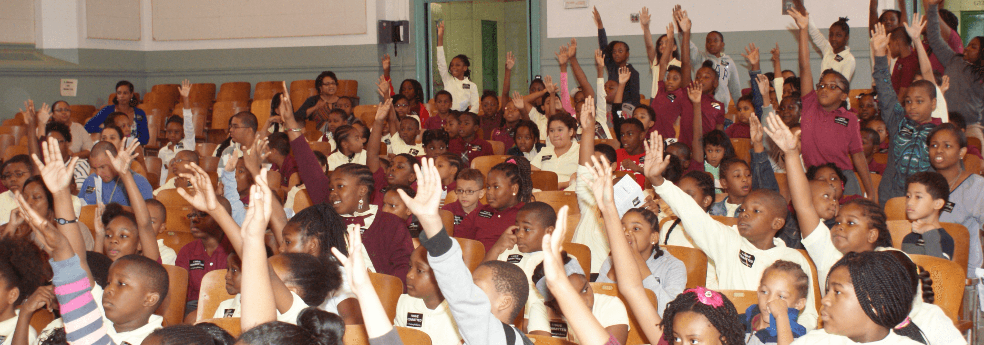 Auditorium full of kids raising their hands