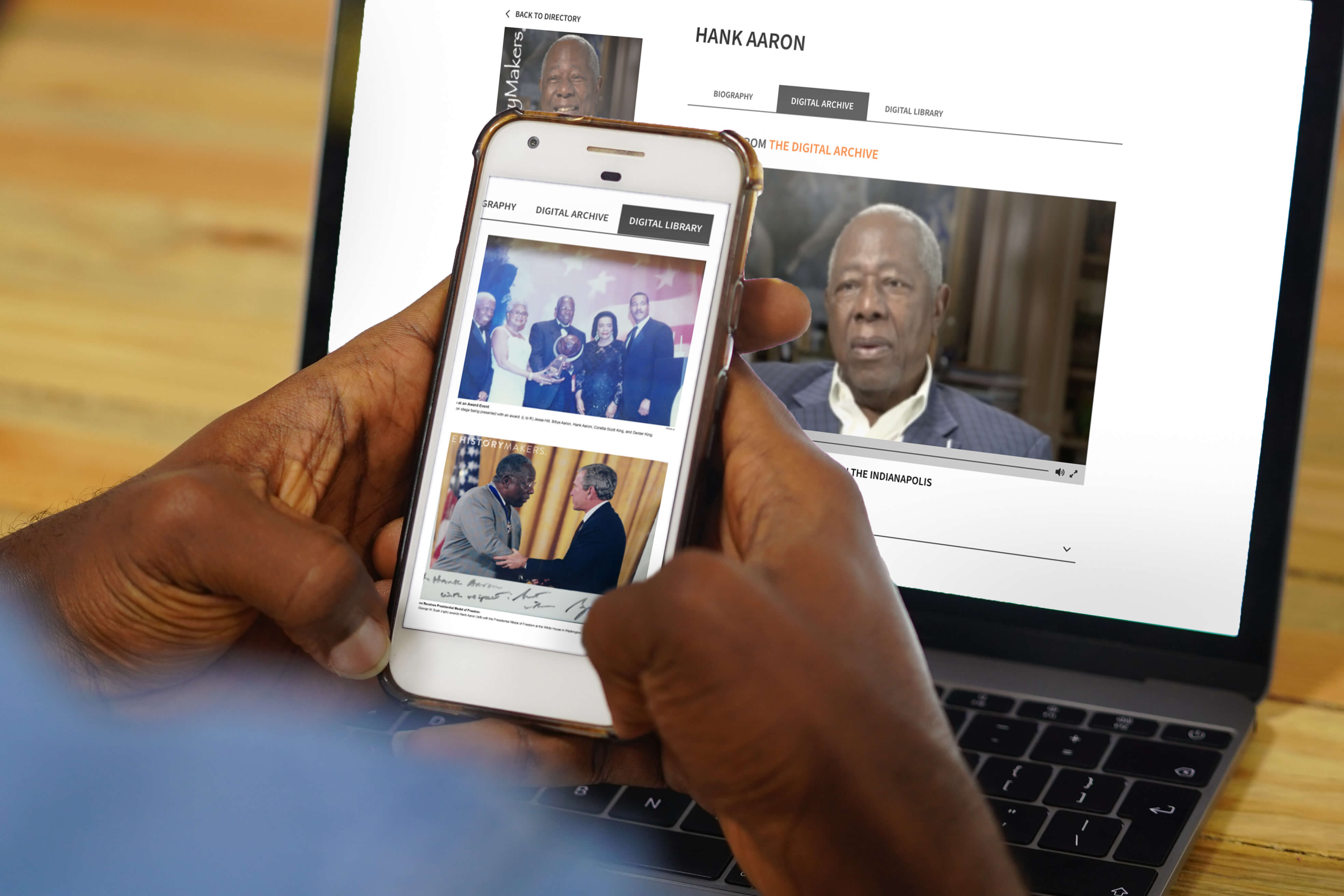 Person looking at The HistoryMakers website on their phone while Hank Aaron's profile is on their laptop screen